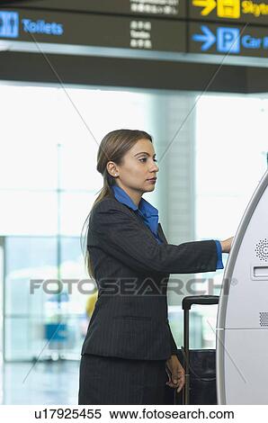 Stock Photography - Side profile of a businesswoman using an automatic ticket machine. Fotosearch