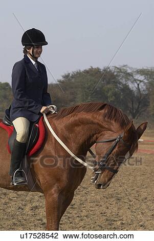 Stock Image - Side profile of a female jockey riding a horse. Fotosearch