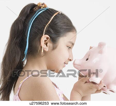 Stock Image - Side profile of a girl holding a piggy bank. Fotosearch