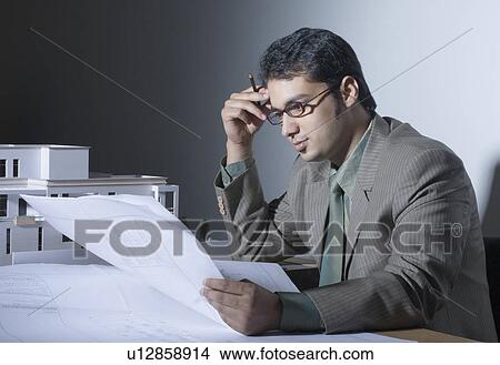 Side profile of a male architect looking at a blueprint and thinking View Large Photo Image Picture - Side profile of a male architect looking at a blueprint and thinking. Fotosearch
