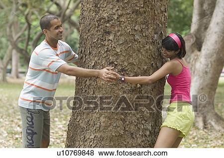 Side profile of a young couple running around a tree View Large Photo Image Stock Photo - Side profile of a young couple running around a tree. Fotosearch