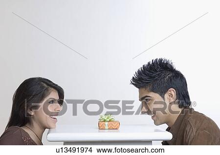 Side profile of a young couple sitting at a table with a present on it View Large Photo Image Picture - Side profile of a young couple sitting at a table with a present on it. Fotosearch
