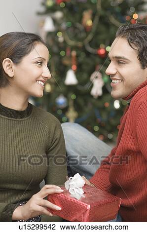 Stock Image - Side profile of a young man giving a Christmas present to a young woman. Fotosearch
