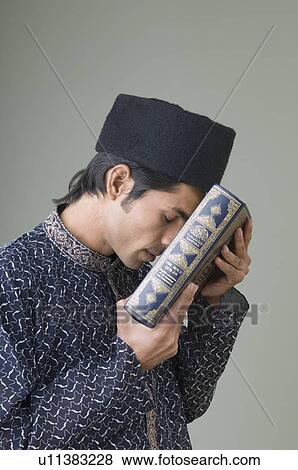 Side profile of a young man holding the Koran against his forehead View Large Photo Image Stock Photo - Side profile of a young man holding the Koran against his forehead. Fotosearch