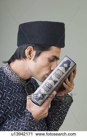 Stock Image - Side profile of a young man kissing the Koran. Fotosearch