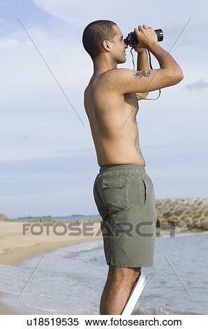 Stock Photography - Side profile of a young man looking through a pair of binoculars. Fotosearch