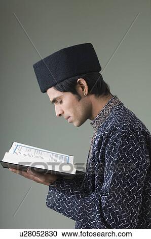 Stock Image - Side profile of a young man reading the Koran. Fotosearch