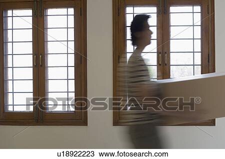 Stock Image - Side profile of a young man walking and carrying a box. Fotosearch