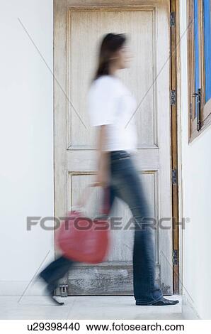 Side profile of a young woman carrying a hand bag and walking out of a room View Large Photo Image Stock Image - Side profile of a young woman carrying a hand bag and walking out of a room. Fotosearch
