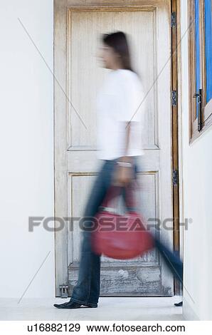 Stock Photo - Side profile of a young woman carrying a hand bag and walking out of a room. Fotosearch
