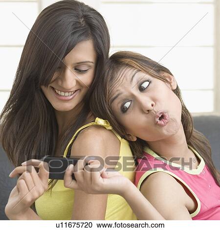 Stock Image - Side profile of a young woman taking a mobile phone from her friend. Fotosearch