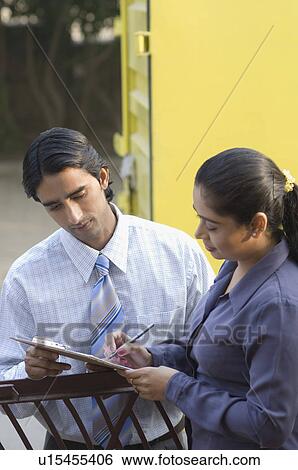 Stock Photograph - Side profile of a young woman writing on a clipboard with a delivery man beside her. Fotosearch