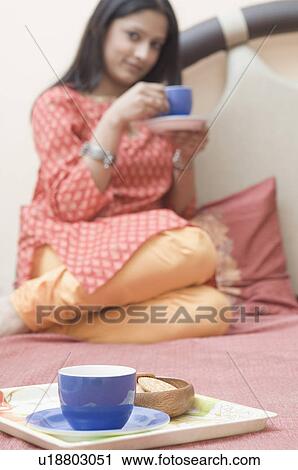 Tea cup on a tray with a young woman drinking a cup of tea in the background View Large Photo Image Stock Image - Tea cup on a tray with a young woman drinking a cup of tea in the background. Fotosearch