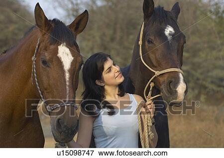 Stock Photo - Teenage girl standing with her two horses. Fotosearch