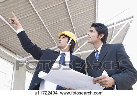Two architects discussing a blueprint at a construction site View Large Photo Image Picture - Two architects discussing a blueprint at a construction site. Fotosearch