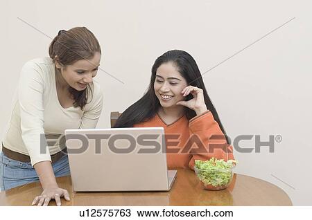 Stock Image - Two young women using a laptop and smiling. Fotosearch