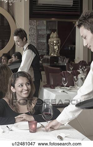 Stock Photo - Waiter serving a glass of red wine to a young woman in a restaurant. Fotosearch