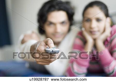 Stock Photo - Young couple lying on a bed and watching television. Fotosearch