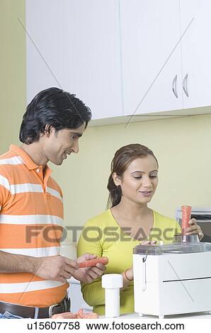 Stock Photo - Young couple making carrot juice in a kitchen. Fotosearch