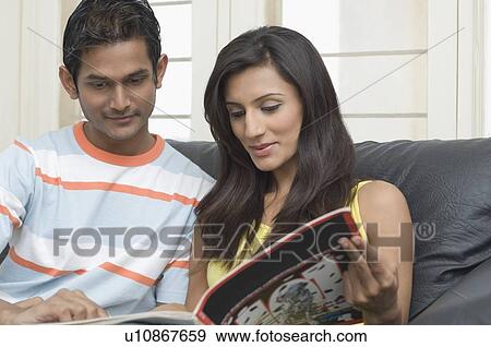 Stock Photo - Young couple sitting on a couch and reading a magazine. Fotosearch