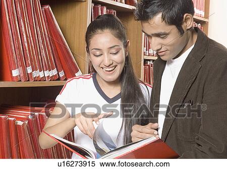 Stock Photography - Young man and a young woman reading a book in a library. Fotosearch