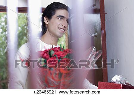 Young man holding a bouquet of flowers and a present View Large Photo Image Stock Image - Young man holding a bouquet of flowers and a present. Fotosearch