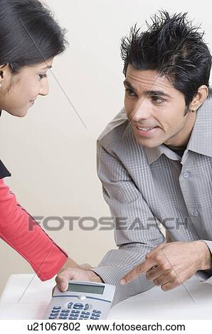 Stock Image - Young man pointing at a calculator with a young woman beside him. Fotosearch
