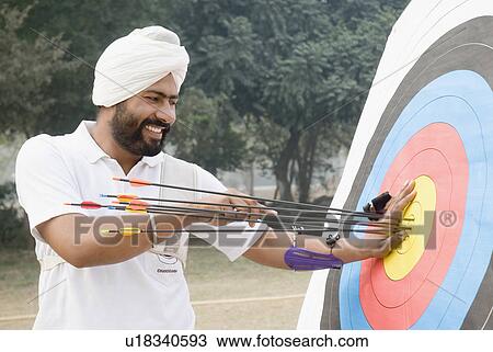 Stock Image - Young man pulling an arrow from a bull's-eye and smiling. Fotosearch