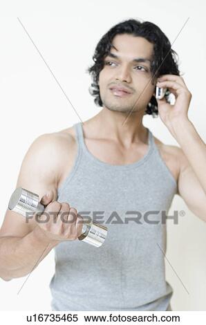 Young man talking on a mobile phone and holding a dumbbell View Large Photo Image Stock Photography - Young man talking on a mobile phone and holding a dumbbell. Fotosearch