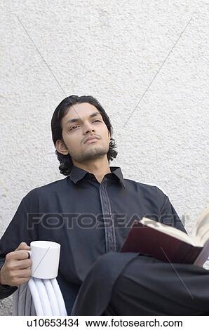 Picture - Young man thinking and holding a cup of tea. Fotosearch
