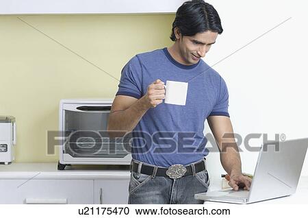 Young man using a laptop and holding a cup of coffee View Large Photo Image Stock Image - Young man using a laptop and holding a cup of coffee. Fotosearch