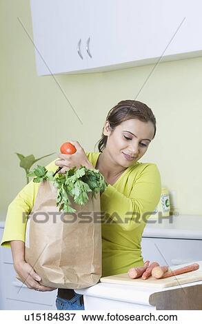 Stock Photo - Young woman carrying a bag of vegetables and smiling. Fotosearch