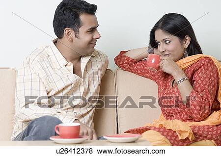 Young woman drinking a cup of tea with a young man looking at her View Large Photo Image Stock Photo - Young woman drinking a cup of tea with a young man looking at her. Fotosearch