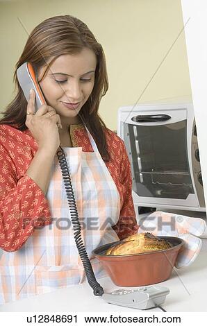 Young woman holding a cake in a mould and talking on a telephone View Large Photo Image Stock Image - Young woman holding a cake in a mould and talking on a telephone. Fotosearch