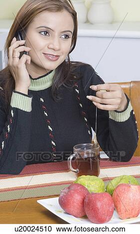 Young woman holding a tea bag and talking on a mobile phone View Large Photo Image Stock Image - Young woman holding a tea bag and talking on a mobile phone. Fotosearch