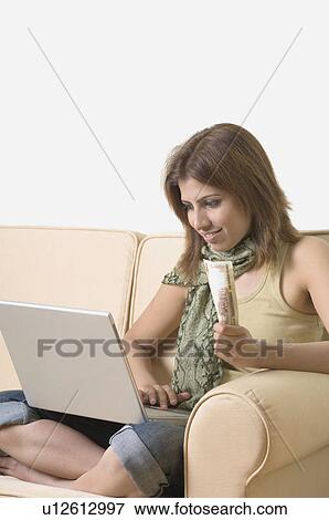 Young woman holding money and using a laptop View Large Photo Image Stock Photo - Young woman holding money and using a laptop. Fotosearch