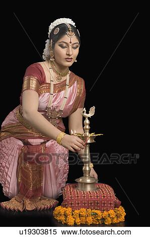 Stock Photography - Young woman kneeling and holding a ceremonial lamp. Fotosearch