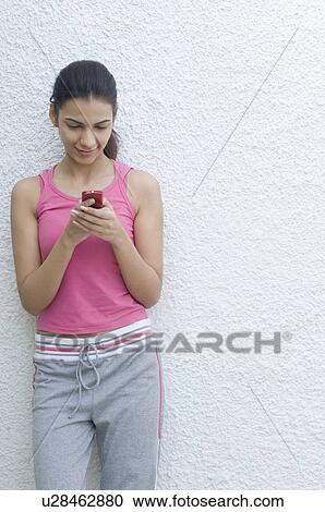 Young woman leaning against a wall and holding a mobile phone View Large Photo Image Stock Image - Young woman leaning against a wall and holding a mobile phone. Fotosearch