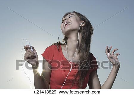 Stock Photo - Young woman listening to an MP3 player and laughing. Fotosearch