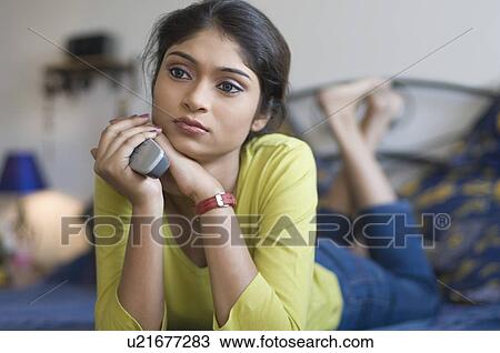 Young woman lying on a bed and holding a remote control View Large Photo Image Stock Image - Young woman lying on a bed and holding a remote control. Fotosearch
