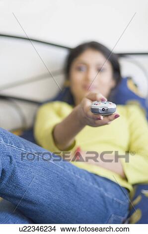 Young woman lying on the bed and using a remote control View Large Photo Image Picture - Young woman lying on the bed and using a remote control. Fotosearch