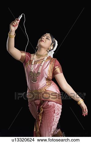 Picture - Young woman performing Bharatnatyam and listening to an MP3 player. Fotosearch