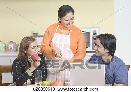 Stock Photo - Young woman pouring milk into a glass for a young couple in a kitchen. Fotosearch