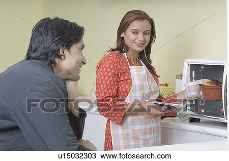Young woman putting a cake into the oven with a young man looking at her View Large Photo Image Stock Image - Young woman putting a cake into the oven with a young man looking at her. Fotosearch