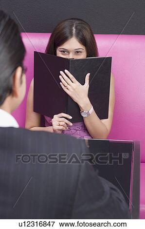 Stock Photo - Young woman sitting in front of a young man and holding a menu. Fotosearch