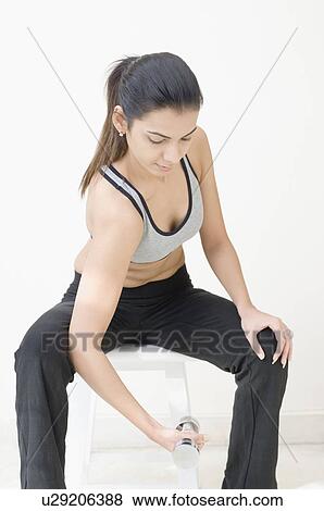 Young woman sitting on a stool and exercising with dumbbells View Large Photo Image Stock Photo - Young woman sitting on a stool and exercising with dumbbells. Fotosearch