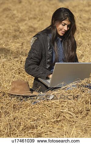 Stock Photo - Young woman sitting on the field and using a laptop. Fotosearch