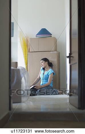 Stock Image - Young woman sitting on the floor and talking on a telephone. Fotosearch