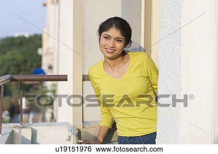 Young woman standing at the balcony and smiling View Large Photo Image Stock Photograph - Young woman standing at the balcony and smiling. Fotosearch