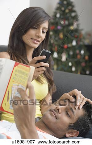 Young woman talking on a mobile phone beside a young man reading a book View Large Photo Image Stock Photo - Young woman talking on a mobile phone beside a young man reading a book. Fotosearch